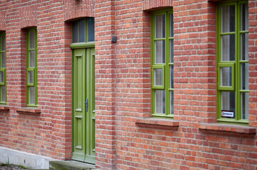 Fototapeta premium A row of green-framed windows and a door set against a red brick building, highlighting the architecture and the contrast between the bright green and earthy red tones.