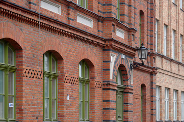Detail view of vintage green windows and door against a red-brick building in Księży Młyn, showcasing restored architectural features in Łódź © sebastiangora