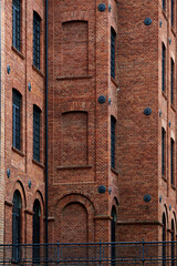 A vertical brick wall of a historic industrial building, showcasing a pattern of bricked-up windows...