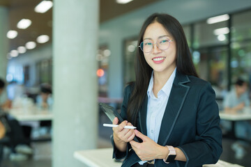 Happy successful female bank manager or businesswoman or female entrepreneur holding digital tablet standing in modern office workplace.
