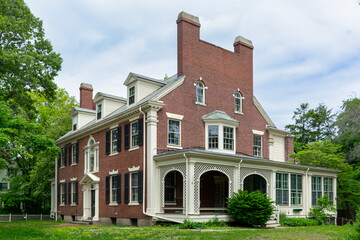 Elegant red brick mansion with classical detailing and wraparound porch in lush greenery in Brookline, Massachusetts, USA
