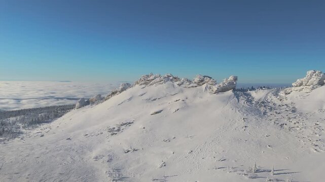 Drone glides along a wind-carved rock ridge above the taiga of Sheregesh, crystalline snow covering the plateau under a cloudless sky. Massive blocks and cornice detail add drama and geologic scale