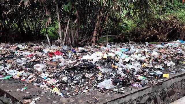 Pile of mixed plastic waste, food wrappers, and household garbage dumped in an open area near a drainage channel, showing environmental pollution and improper waste management.