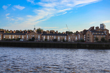 Row of Elegant Waterfront Buildings on the river bank with Blue Sky and Reflections in Central London