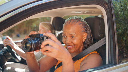 Passenger Taking Photo On Digital Camera As Two Senior Female Friends Enjoy Day Trip Out In Car