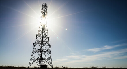 This dramatic image features the silhouette of a modern telecommunications tower or cell phone mast against a brilliant blue sky. The sun bursts directly from behind the tower