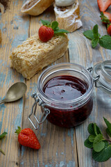 strawberry jam in a small jar on a wooden background with a cake