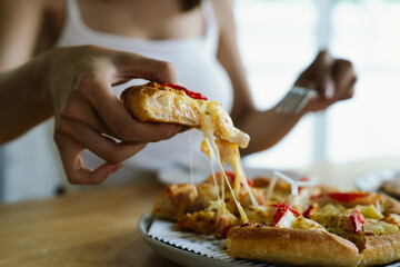 woman enjoys a freshly baked pizza with cheese, crab sticks and pineapple on a wooden table, ready to be served.