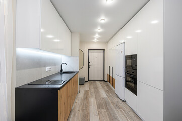 modern kitchen featuring white cabinets, a black countertop with a wooden base, sleek appliances, and light wood-patterned flooring. The design is minimalist and bright