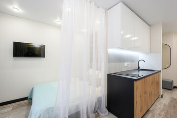 compact studio apartment featuring a bed separated by sheer white curtains and a modern kitchenette