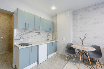 modern kitchen features light blue cabinets, a white marble backsplash, and a small dining table with gray chairs. The walls are decorated with patterned wallpaper