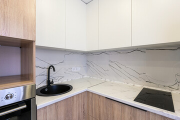 modern kitchen features white and wood cabinets, a black sink and faucet, and a marble countertop and backsplash