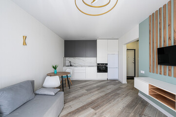 modern living room featuring a gray sofa, a small dining table, and a sleek kitchen. TV on the wall with wooden decor accents