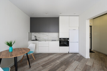 modern kitchen with white cabinets, gray upper cabinets, a marble backsplash, and a wood floor. A round table sits beside it