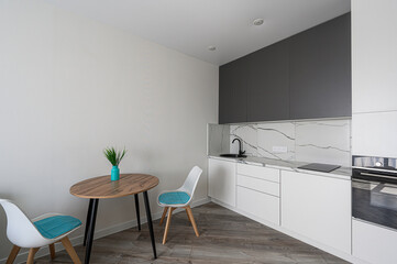 Modern kitchen interior featuring gray and white cabinets, marble backsplash, a wooden table with two chairs, and a turquoise vase