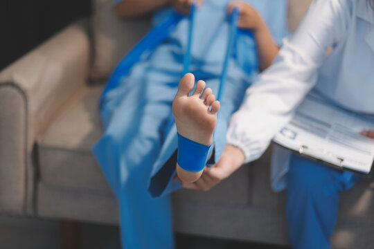 Confident physical therapist helps patient use resistance band stretching out his leg in clinic room.