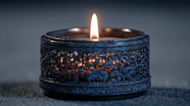 Lit candle in intricate dark holder, casting glow through ornate floral lattice pattern