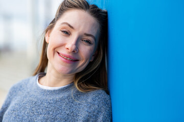 Close up portrait smiling young woman leaning against blue wall outdoors