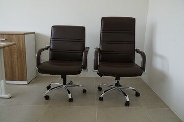 Two brown leather office chairs sit side by side on a tiled floor