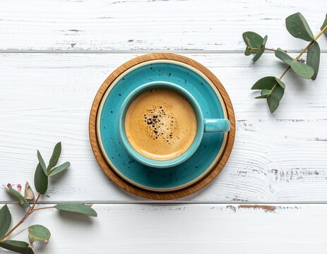 Teal handmade pottery hot coffee mug on wooden coaster on white rustical table flatlay. 