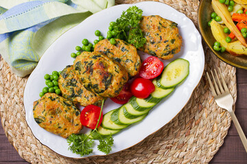 Chicken spinach burgers with green peas and vegetables on white plate. View from above, top studio shot