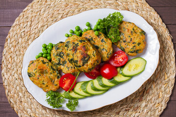 Chicken spinach burgers with green peas and vegetables on white plate. View from above, top studio shot