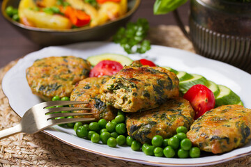 Chicken spinach burgers with green peas and vegetables on white plate