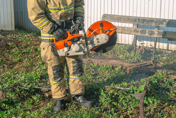 A lifeguard in protective clothing holds a gas cutter with a cutting wheel. A firefighter in a...