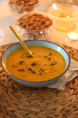 Plate of pumpkin soup, pumpkins, glass of wine, nuts and lit candles on the table. Selective focus.