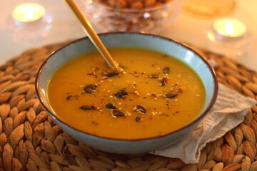 Plate of pumpkin soup, pumpkins, glass of wine, nuts and lit candles on the table. Selective focus.