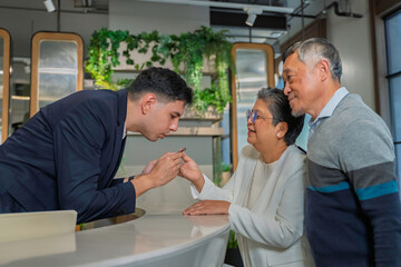 Obraz premium Friendly concierge assisting senior couple at modern hotel reception desk, providing direction with warm service and welcoming hospitality in a stylish urban environment.