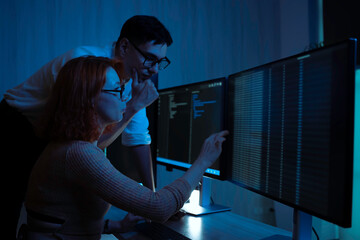 Two software developers collaborating at night, focusing on code review and debugging process on a computer screen, representing teamwork, innovation, and modern software development workflow.