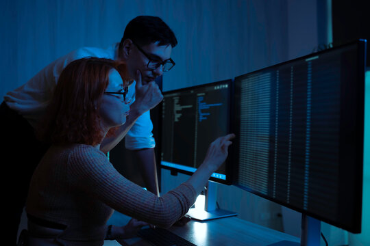 Two software developers collaborating at night, focusing on code review and debugging process on a computer screen, representing teamwork, innovation, and modern software development workflow. - Powered by Adobe