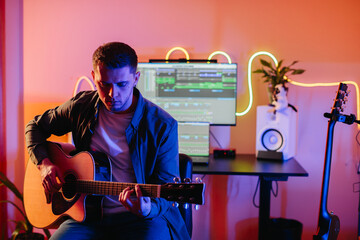 Musician composing new song playing acoustic guitar and using music production software