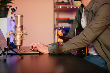 Musician composing music on laptop with guitar and microphone