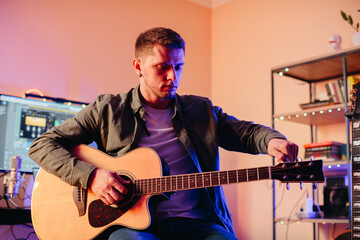 Obraz premium Musician tuning acoustic guitar and recording music at home studio