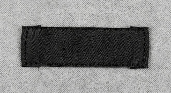Blank black fabric label stitched onto a textured grey non-woven textile background, offering copy space for branding or text.