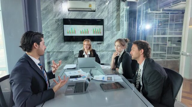 Business Meeting in Modern Office: Four business professionals are seated around a conference table in a contemporary office space.