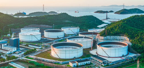 Large white oil storage tanks situated on a green coastal hillside.