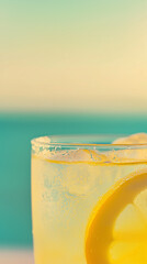 Close-up of a chilled glass of lemonade with ice and a lemon slice, set against a soft, sunlit seaside background