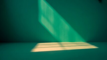 A bright beam of light from a window shines on a teal wall and floor. The resulting contrast creates an interesting interplay of light and shadow.