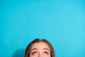 Young woman looking up with curious expression against bright blue background, conveying contemplation and youth