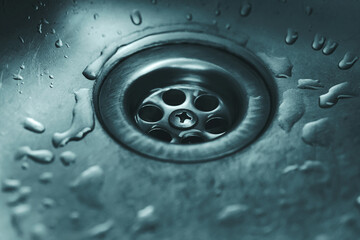 A close-up of a clean metal sink drain with water droplets and a moody blue tone, highlighting plumbing, hygiene, and modern design.