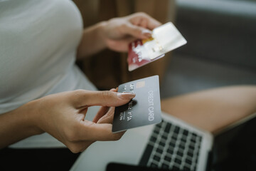 A young woman uses her smartphone and holds credit cards while sitting indoors, representing online shopping, finance, technology, and e-commerce.