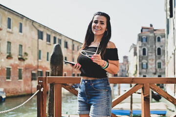 Happy smiling beautiful  Tourist  woman traveling at   Venice Italy, poses and making photos   against colorful houses. Concept of Italian gastronomy and travel. 