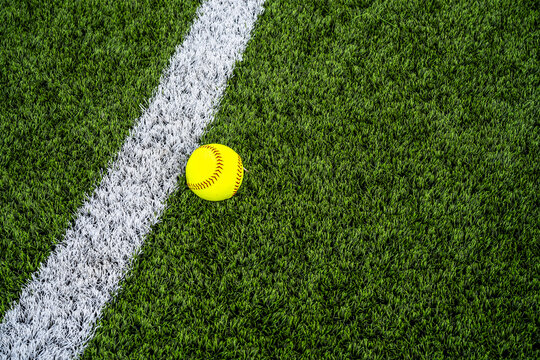 Close-up of a classic softball with red stitching resting on the turf, symbolizing sport, teamwork, competition, and outdoor athletic activity in high detail.