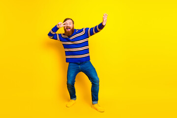 Cheerful bearded man in vibrant striped sweater posing energetically against a lively yellow background