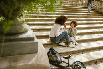 A son sits on a blanket on the stairs next to his mother while they eat ice cream