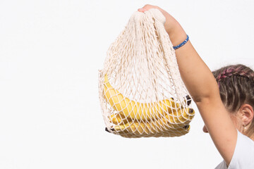 Obraz premium a teenage girl holds bananas in a net on a white background,