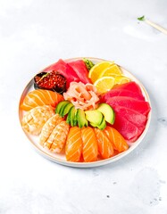 Round platter of assorted sushi and sashimi, featuring salmon, tuna, and shrimp, garnished with ginger, avocado, and citrus